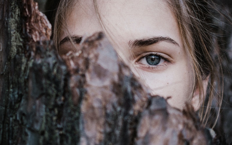 girl's face partially hidden behind a piece of wood.