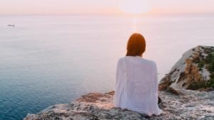 back of woman on rock cliff facing ocean