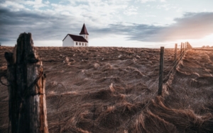 barren field, broken down fence and a white church with a steeple far off in the field 