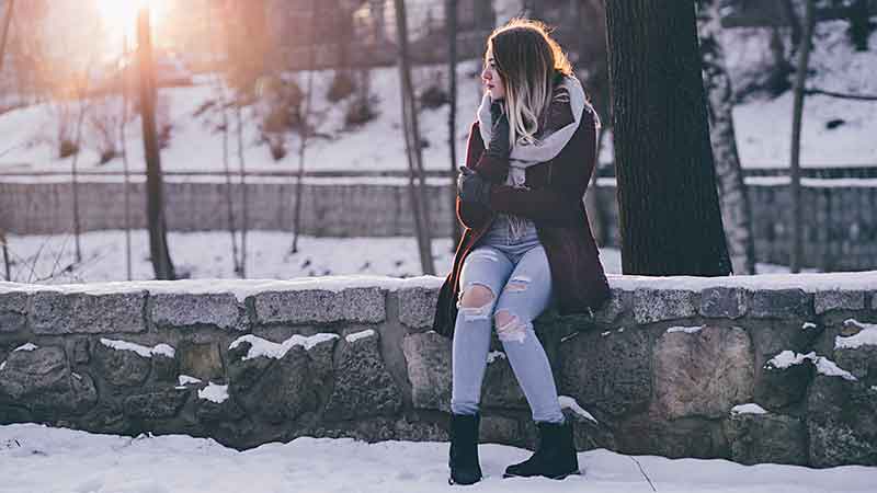 young woman sitting on stone wall in snow