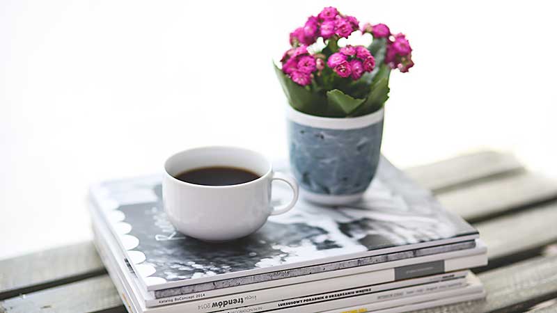 coffee cup and flowers on top of magazines