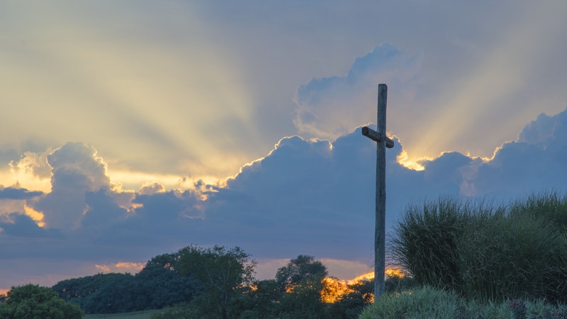 Cross on hilltop sun shining behind clouds