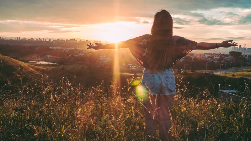 girl in field arms out facing sunrise