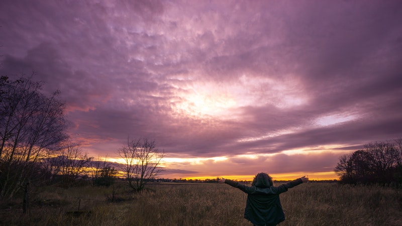 woman in field, arms up facing sunset