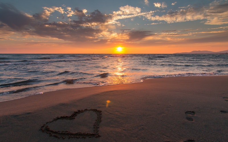 sunset beach with heart drawn in sand