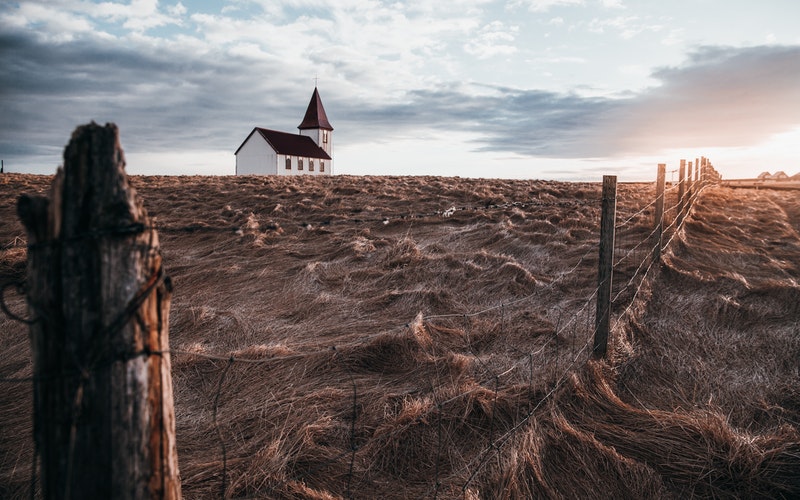 barren field, broken down fence and a white church with a steeple far off in the field