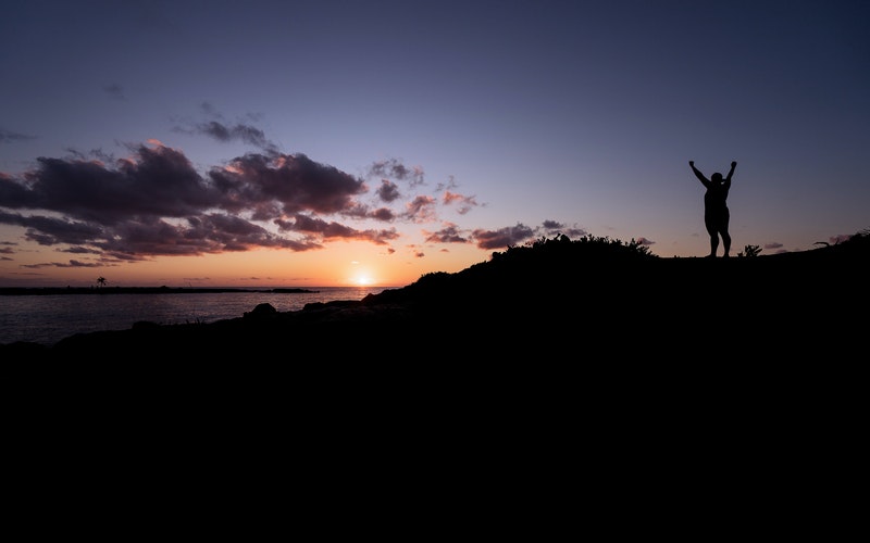 sunsetting over a mountain, silhouette of woman with hands raise. His Finish Line