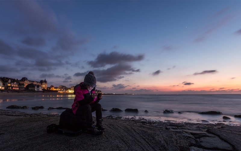 woman on shoreline in jacket, hat holding cellphone and reading it. Social media and the Heart