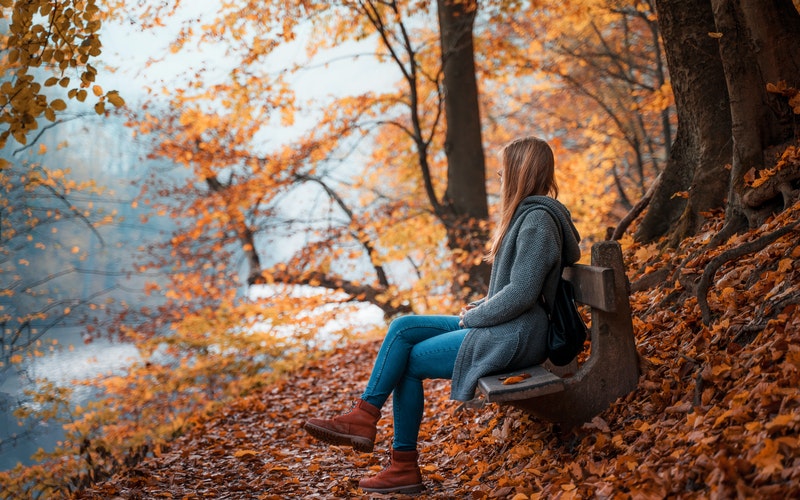 girl sitting on a bench looking away with fall leaves covering the ground in falling from the trees Investing in Relationship