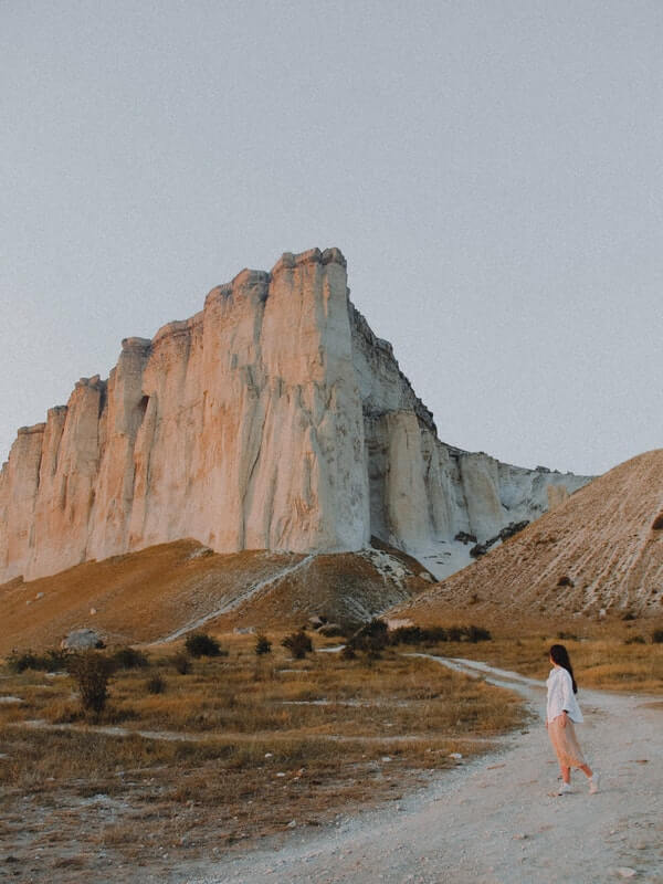 Woman in the forefront walking on desolate road, rock mountains in background. Blog post Abandonment